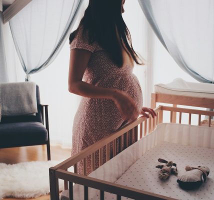 woman in white lace sleeveless dress standing beside brown wooden crib