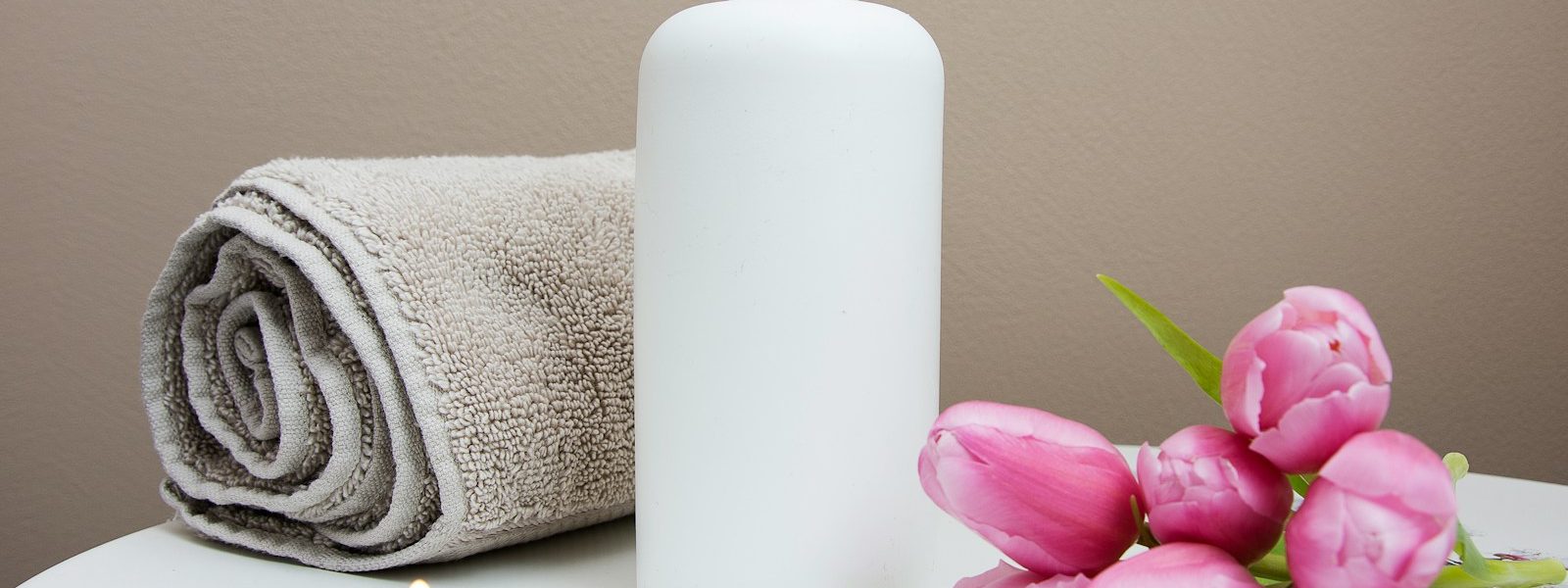 white plastic pump bottle beside pink tulips and gray towel
