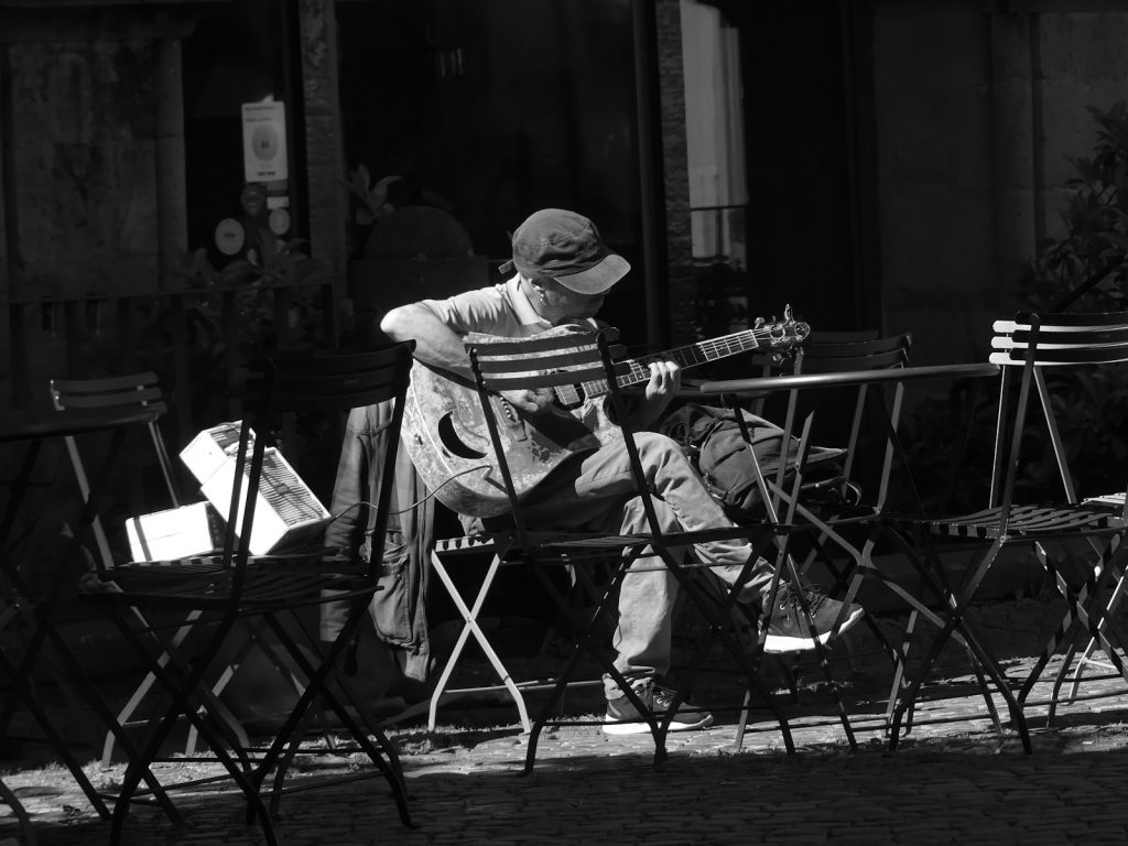 A person plays guitar at an outdoor cafe table.