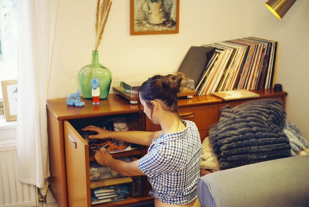 A woman kneeling to organize cables inside a teak cabinet with vinyl records above
